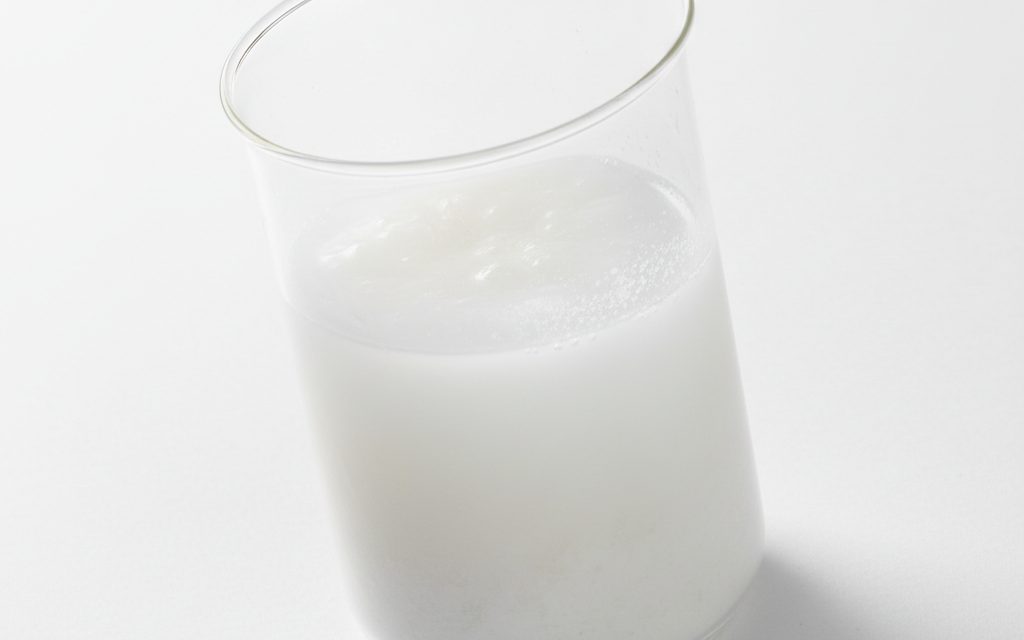 Grade confirmed at quotation — fine, odorless, soft white powder; forms a milky, chalky suspension when mixed with water in a lab dish, studio product photograph