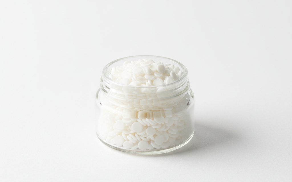 Grade confirmed at quotation — white, smooth waxy granules or flakes with a neutral odor, providing a non-greasy feel in solid bulk form, studio product photograph