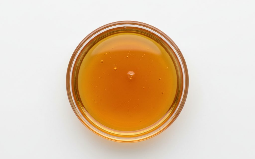 Grade confirmed at quotation — clear, viscous amber-colored liquid with a mild, slightly nutty chemical odor, possessing a syrupy and oily physical texture, studio product photograph