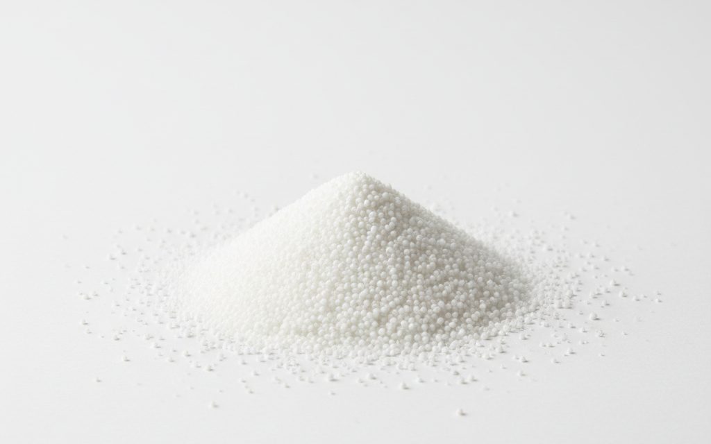 Grade confirmed at quotation — tiny, spherical white beads or granules containing a blowing agent, appearing similar to fine sugar or sand, studio product photograph