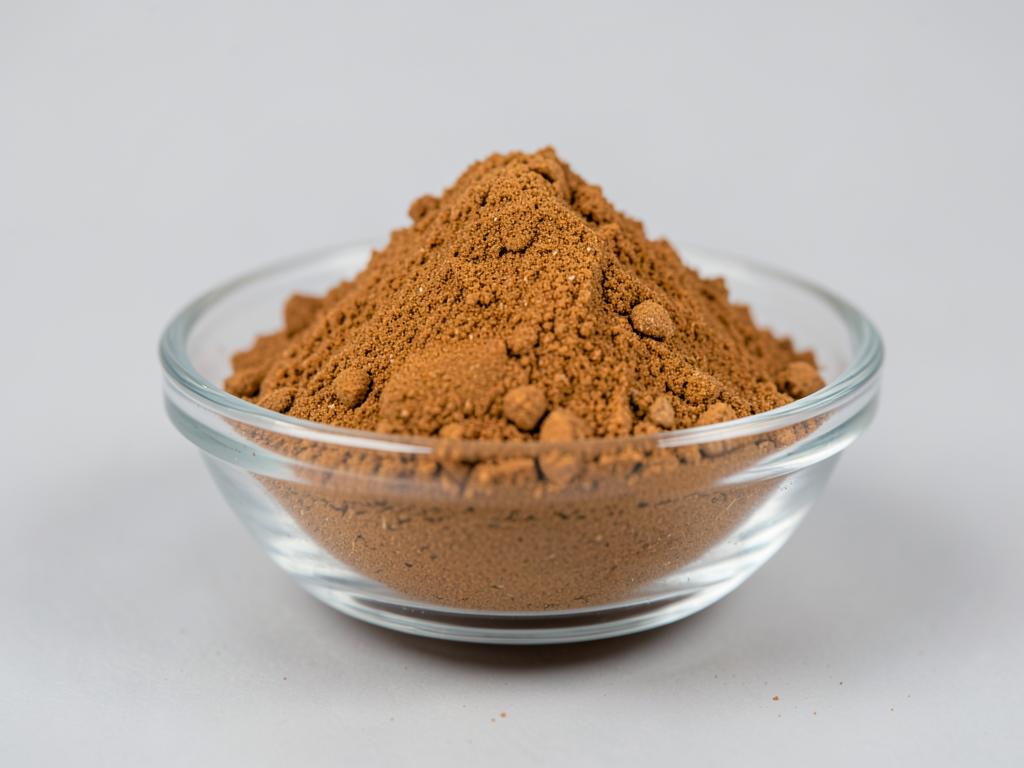 Haritaki Powder shown as a dried milled botanical powder in a shallow dish in a neutral studio photograph