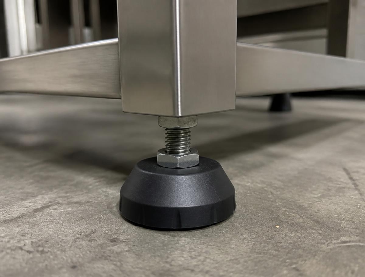 Stainless steel machine frame leg resting on a black plastic levelling foot adjusted with a lock nut on a concrete floor