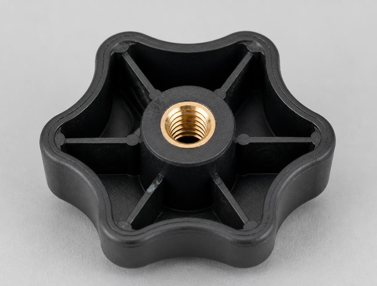 Underside of a black plastic star knob showing the brass threaded insert moulded into the central boss