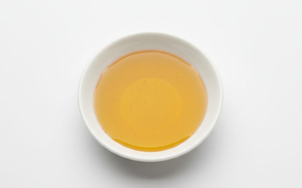 Grade confirmed at quotation — a viscous, amber to golden-yellow oily liquid with a distinctive, slightly bitter aroma and high clarity, studio product photograph