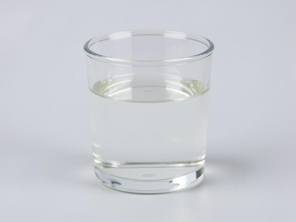 Potassium lactate shown as a clear colourless liquid in a plain glass vessel in a neutral studio photograph