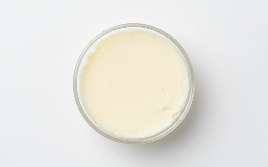 Grade confirmed at quotation — an off-white to pale yellow, solid fatty butter with a smooth, grainy, or slightly waxy texture, studio product photograph