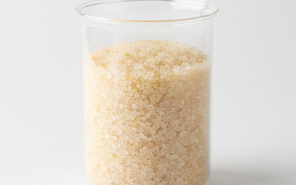 Grade confirmed at quotation — light yellow to pale orange monoclinic crystals or powder, often appearing as fine, free-flowing grains for industrial salt treatment, studio product photograph