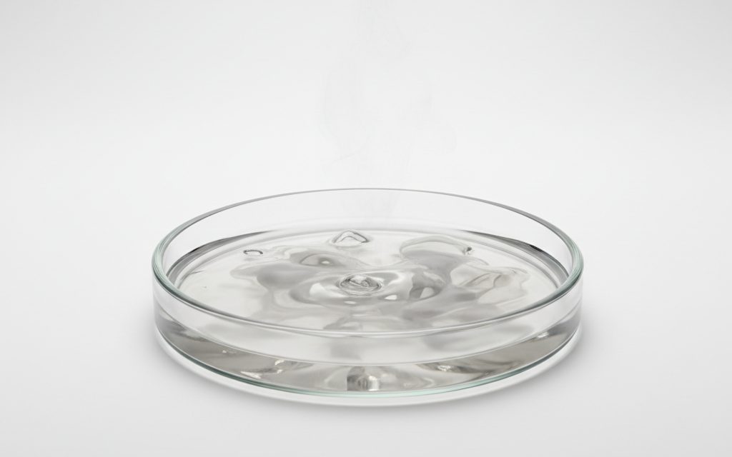 Grade confirmed at quotation — clear, colorless to cloudy gray, oily, heavy liquid; noticeably dense and viscous, generating significant heat when diluted in beakers, studio product photograph