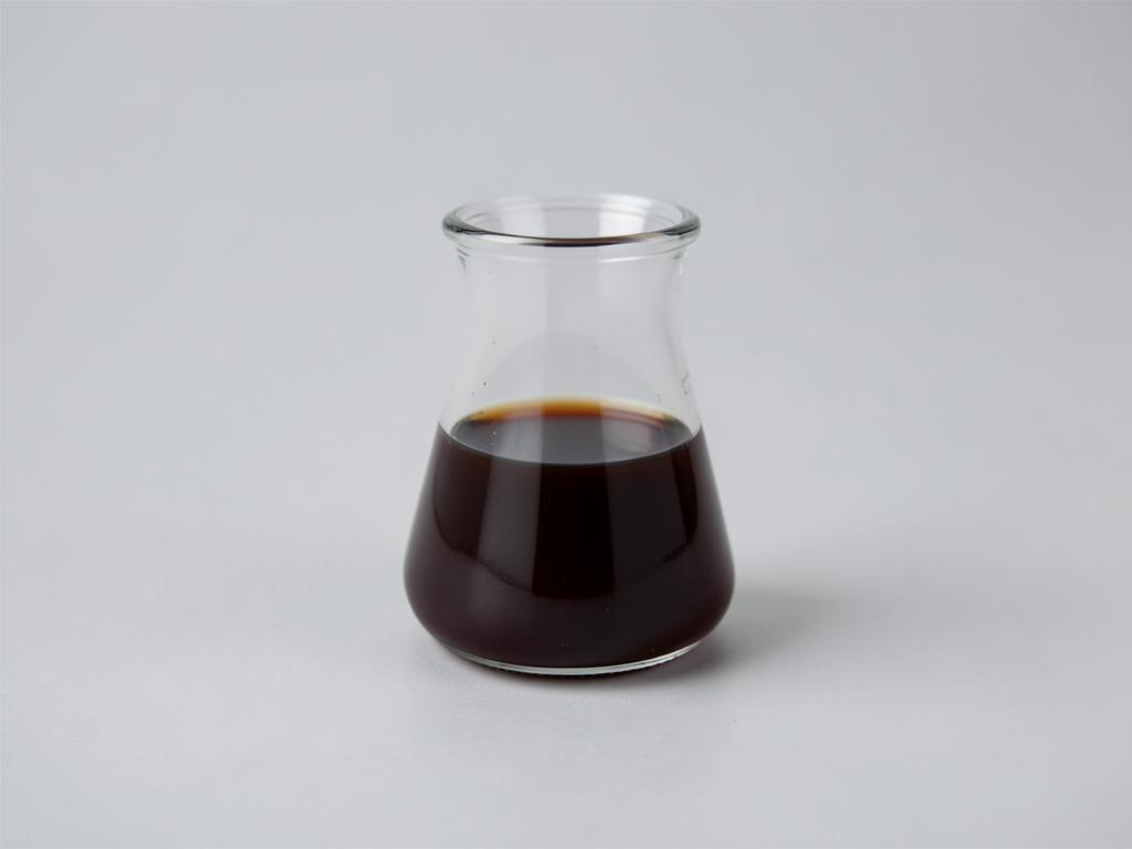 Vanilla extract shown as a dark brown liquid in a clear glass beaker in a neutral studio photograph