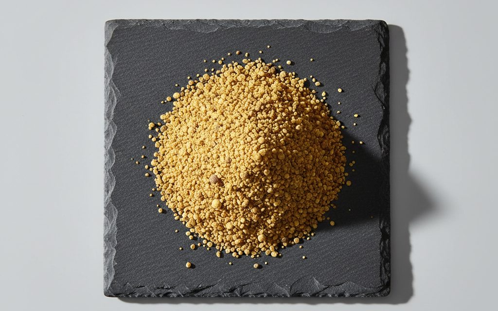 Vitamin A Acetate — yellow to brownish free-flowing beadlets or fine spherical granules, often starch-coated to provide a dry, non-clumping tactile feel, studio product photograph